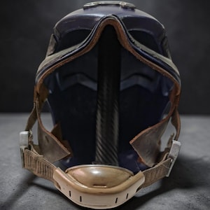 K&ouml;nnte beinhalten: Nahaufnahme eines futuristischen Helms. Der Helm ist &uuml;berwiegend dunkelblau mit braunen Lederbes&auml;tzen und Riemen. Er hat ein Visier und einen Kinnriemen mit einem beigefarbenen Polster. Der Innenraum ist dunkelblau.