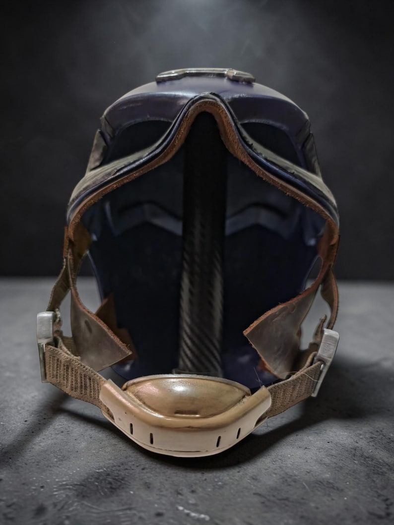 K&ouml;nnte beinhalten: Nahaufnahme eines futuristischen Helms. Der Helm ist &uuml;berwiegend dunkelblau mit braunen Lederbes&auml;tzen und Riemen. Er hat ein Visier und einen Kinnriemen mit einem beigefarbenen Polster. Der Innenraum ist dunkelblau.