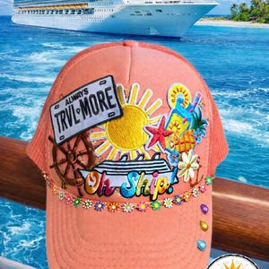 Puede incluir: Gorra de camionero coral con parte trasera de malla y temática de crucero. La gorra presenta parches bordados de un sol, una estrella de mar y las palabras "TRVL MORE" y "Oh Ship!". Un crucero es visible en el fondo.