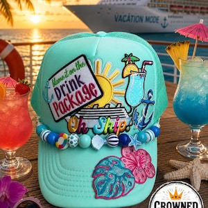 Puede incluir: Una gorra trucker de color turquesa claro con un parche que incluye el texto "Blame it on the Drink Package" y "Oh Ship", un sol amarillo, un cóctel azul y un ancla. La gorra está decorada con un borde de cuentas y parches de hojas y flores.