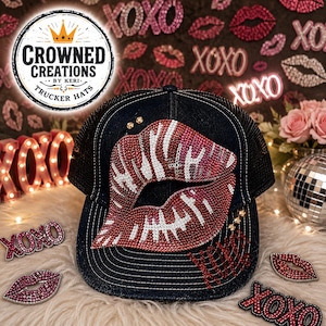 Puede incluir: Una gorra de camionero negra con un gráfico central grande de labios adornado con pedrería roja, blanca y rosa. La gorra incluye el texto CROWNED CREATIONS BY KERI TRUCKER HATS en un logotipo circular en la esquina superior izquierda.