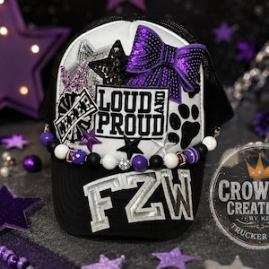 May include: A black and white trucker hat featuring a purple sequin bow, star appliques, and a patch with the text LOUD AND PROUD. The brim displays the letters FZW in silver, and a beaded strand with purple, black, and white beads encircles the crown.