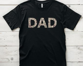 Op de afbeelding: Zwart T-shirt met het woord "DAD" in camouflagepatroon.