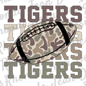 May include: A football with a camouflage pattern in shades of brown, tan, and green, set against the word "TIGERS" in a stacked design. The text is in a blocky font, with the word repeated in different shades.