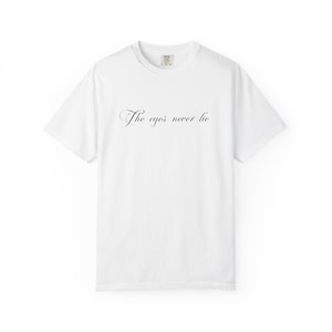 May include: A white short-sleeve t-shirt featuring the black text "The eyes never lie" printed in a cursive script across the center of the chest. The garment has a crew neckline and a standard fit, with a small brand label visible at the inner neck.