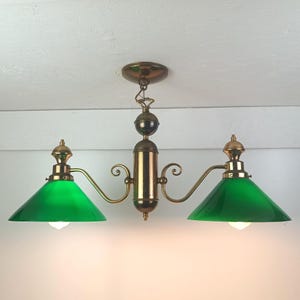 May include: A two-light ceiling fixture featuring a polished brass central column and curved arms supporting two conical green glass shades. The fixture includes a circular brass ceiling canopy and decorative finials at the top of each shade.