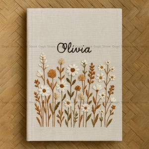 Könnte beinhalten: Ein beiges Leinenjournal mit einem gestickten Blumendesign. Das Cover zeigt weiße Gänseblümchen, braune Stiele und den Namen "Olivia" in Schreibschrift. Das Journal ist ein personalisierter Artikel.