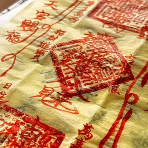 May include: A close-up shot of yellow paper adorned with red Chinese characters and stamps. The paper has a textured, crinkled appearance, with several rectangular stamps and flowing lines of text. The image evokes a sense of tradition and artistry.