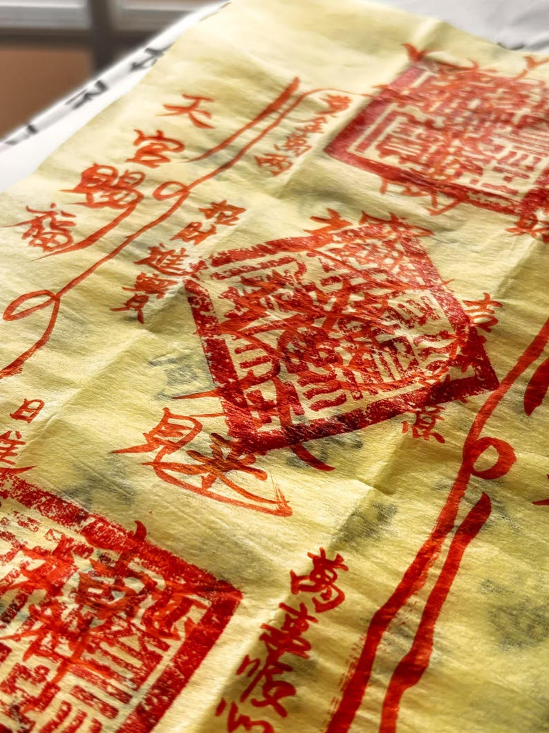 May include: A close-up shot of yellow paper adorned with red Chinese characters and stamps. The paper has a textured, crinkled appearance, with several rectangular stamps and flowing lines of text. The image evokes a sense of tradition and artistry.
