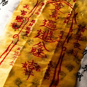 May include: A close-up of a gold-coloured paper with red Chinese characters and symbols. The paper is slightly crumpled and has a textured appearance. The background is a white paper with black Chinese characters.