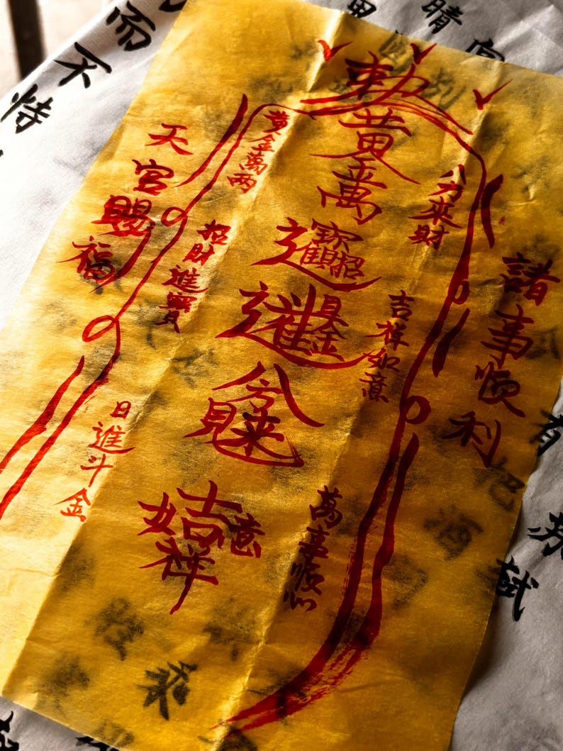 May include: A close-up of a gold-coloured paper with red Chinese characters and symbols. The paper is slightly crumpled and has a textured appearance. The background is a white paper with black Chinese characters.