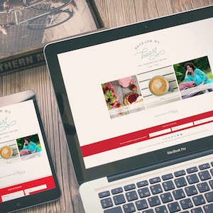 Op de afbeelding: Een laptop en een tabletcomputer die een website weergeven met de titel "Beneath My Heart" en een rood-wit kleurenschema. De website bevat afbeeldingen van eten, drinken en een vrouw. De tekst "Sign up for the Blog" is zichtbaar op de website.