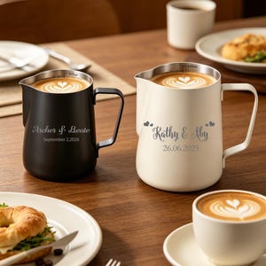 Peut inclure: Deux pichets à latte art personnalisés, un noir et un crème, avec des noms et des dates gravés. Le pichet noir indique "Archer & Beate, September 2, 2026." Le pichet crème indique "Kathy & Aby, 26.06.2025."