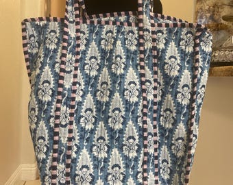 May include: A large tote bag with a blue and white floral pattern. The bag has vertical stripes of navy blue and pink. The handles are made of the same material as the bag. The bag is displayed on a black mannequin.