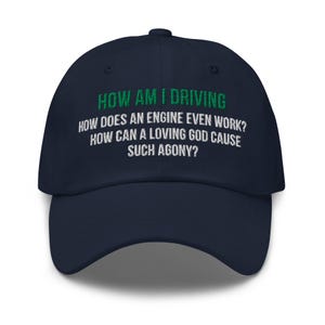 May include: A navy blue baseball cap featuring embroidered text in green and white. The green text reads HOW AM I DRIVING, while the white text below reads HOW DOES AN ENGINE EVEN WORK? HOW CAN A LOVING GOD CAUSE SUCH AGONY? The cap has a curved brim.