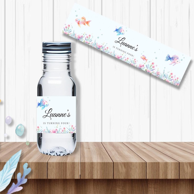 May include: Water bottle label with a blue and pink fish, seaweed, and bubbles. The label says "Luanne's is turning four!"
