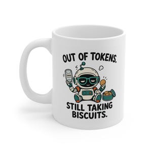 Può includere: Una tazza in ceramica bianca con la grafica di un piccolo robot con occhiali color verde acqua, che tiene in mano un barattolo vuoto con l'etichetta tokens e un biscotto. Il testo recita OUT OF TOKENS. STILL TAKING BISCUITS. Il design usa nero, verde acqua e arancione.