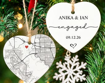 May include: Two white heart-shaped ceramic ornaments hanging from twine. One ornament features a black street map with a small red heart. The other displays the text ANIKA & IAN, engaged, the date 09.12.26, and a small black heart outline.