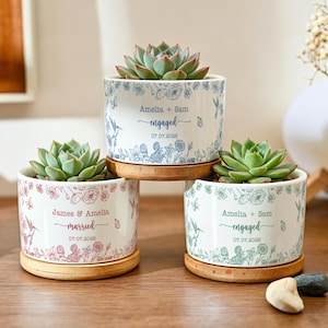 Puede incluir: Tres macetas de cerámica blanca para suculentas con platillos de bambú, cada una con un estampado floral y de colibríes en azul, rosa o verde. Las macetas están personalizadas con nombres, fechas y las palabras engaged o married.