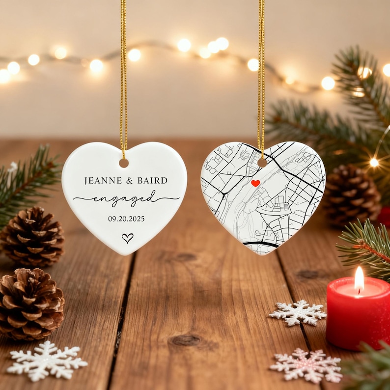 May include: Two heart-shaped ornaments hanging from gold strings. One is white with the words "Jeanne & Baird engaged 09.20.2025" and a heart. The other has a map design with a red heart. Festive holiday decor.
