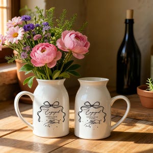 May include: Two white ceramic mugs with handles, each featuring a black line drawing of a bow, the word Engaged, the names Vivian & Oscar, and the date 12.16.2024 above an illustration of two hands reaching toward each other with small stars.
