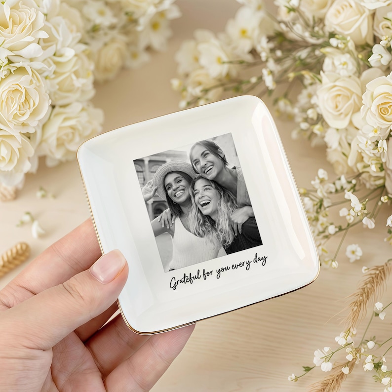Peut inclure: Un vide-poche carr&eacute; en c&eacute;ramique blanche avec un bord dor&eacute;, orn&eacute; d'une photo en noir et blanc de trois personnes souriantes. Le plat porte l'inscription "Grateful for you every day".