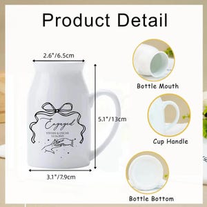 May include: A white ceramic mug with a handle, featuring a black line drawing of a bow, hands exchanging a ring, and the text Engaged, Vivian & Oscar, 12.16.2025. Dimensions are 2.6 inches wide at the mouth, 3.1 inches at the base, and 5.1 inches tall.