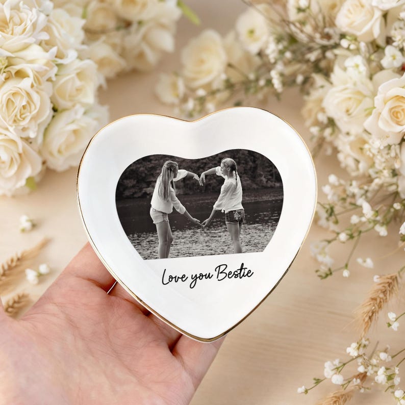 Peut inclure: Un vide-poches en c&eacute;ramique blanc en forme de c&oelig;ur avec un bord dor&eacute;. Le plat pr&eacute;sente une photo en noir et blanc de deux personnes formant un c&oelig;ur avec leurs mains. Les mots "Love you Bestie" sont &eacute;crits sur le plat.