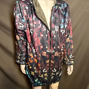 May include: A zip-up hooded jacket featuring a dark, multi-coloured pattern of scattered question marks in shades of blue, red, and yellow. The garment includes a black front zip, a drawstring hood, and a textured, grey faux-fur lining.