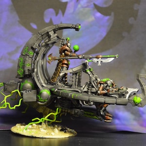 Könnte beinhalten: Eine detaillierte Miniatur eines futuristischen Science-Fiction-Fahrzeugs mit einem grün-grauen Farbschema. Das Fahrzeug hat ein großes, kreisförmiges, offenes Cockpit mit einer Figur auf dem Fahrersitz. Das Fahrzeug hat eine lange, dünne Waffe, die an der Vorderseite befestigt ist.