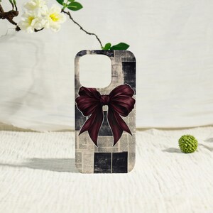 May include: A rectangular smartphone case featuring a background pattern of black and white newspaper print columns. Centered on the case is a large, dark burgundy bow illustration with detailed shading and defined folds throughout the fabric.