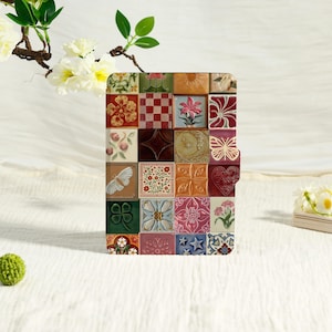 May include: A rectangular e-reader case featuring a grid of colorful tiles with diverse embossed patterns including flowers, a butterfly, a heart, a moon, stars, a clover, and geometric shapes in shades of red, green, blue, and gold.