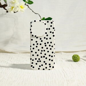 May include: A white phone case with a black polka dot pattern. The case has cutouts for the camera and buttons. The case is made of a smooth material and is designed to protect the phone from scratches and damage.