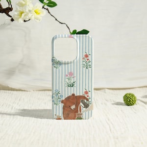 May include: A phone case with a whimsical design. The case features a light blue and white striped background with floral accents. A brown bear is depicted pouring from a teapot. The case is designed to fit a smartphone.