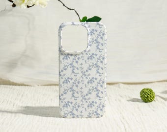 May include: A white phone case with a delicate blue floral pattern. The case has a rectangular shape with rounded corners and a cutout for the camera. The floral design is a repeating pattern of small blue flowers and leaves.