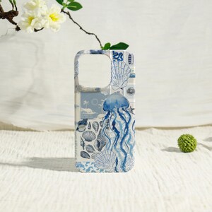 May include: A white and blue phone case featuring a nautical design. The case has illustrations of seashells, a jellyfish, and other sea-themed elements. The design is in shades of blue and white.
