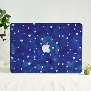 May include: A blue laptop case with a starry night design. The case features a dark blue watercolor background with white stars scattered across the surface. The Apple logo is visible in the center.
