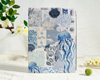 May include: A rectangular notebook with a collage design featuring seashells, jellyfish, and surfboards in shades of blue and white. The notebook is displayed on a white surface with floral accents.