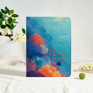 May include: A rectangular tablet case featuring a vibrant underwater scene with colorful coral reefs in shades of orange, pink, and blue. The design includes a school of small orange and white clownfish and a single dark blue fish swimming in water.