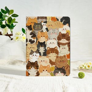 May include: A rectangular case with a vibrant illustration of many cartoon cats. The cats are in various colours, including orange, brown, grey, and black, with different patterns. The background is a light beige colour.