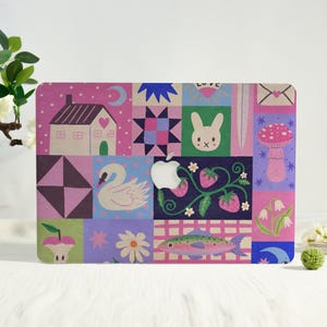 May include: A laptop skin featuring a colorful grid of illustrations including a house, a quilt pattern, a rabbit face, a swan, strawberries on a vine, a mushroom, a fish, flowers, and moons, with a central cutout for an Apple logo.