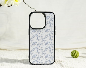 May include: A phone case with a black border and a white background featuring a delicate blue floral pattern. The case has a cutout for the camera and is designed to protect the phone. The case is a stylish accessory.