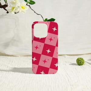 May include: A pink and red checkered phone case with white starburst designs. The case has a glossy finish and is designed to fit a smartphone. The case is a vibrant accessory.