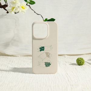 May include: A beige phone case featuring three cartoon cats in various poses. Each cat wears a different patterned outfit in green and white. The case has a cutout for the camera and buttons.