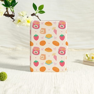 May include: A cream-colored tablet case with a repeating pattern of baked goods and fruit. The design includes strawberries, jam jars, croissants, bread loaves, butter, and cookie illustrations. The case is rectangular and has a smooth surface.