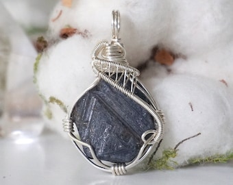 May include: A dark blue gemstone pendant wrapped in silver wire. The pendant is a unique, faceted shape and is set on a silver chain.