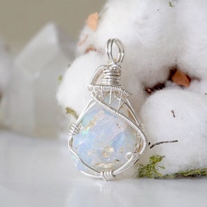 May include: A silver wire wrapped pendant featuring a white opal gemstone. The pendant is a teardrop shape and has a delicate, intricate design.