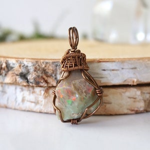 May include: A copper wire wrapped pendant featuring a natural opal gemstone with iridescent colors. The pendant is a unique and handmade piece of jewelry.