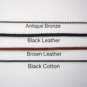 May include: An image showcasing various necklace cord options. The choices include an antique bronze chain, black leather, brown leather, and black cotton cord. Each cord type is labeled with its respective material.