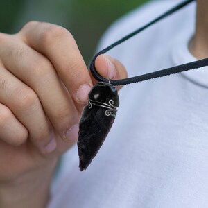 May include: A black leather cord necklace with a black and white arrowhead pendant wrapped in silver wire.